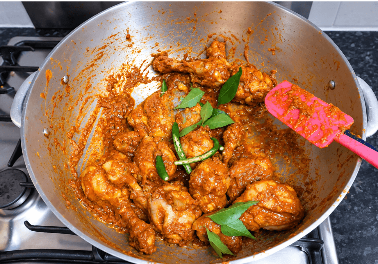 Chicken drumsticks cooking in spicy coconut masala with curry leaves and green chilli