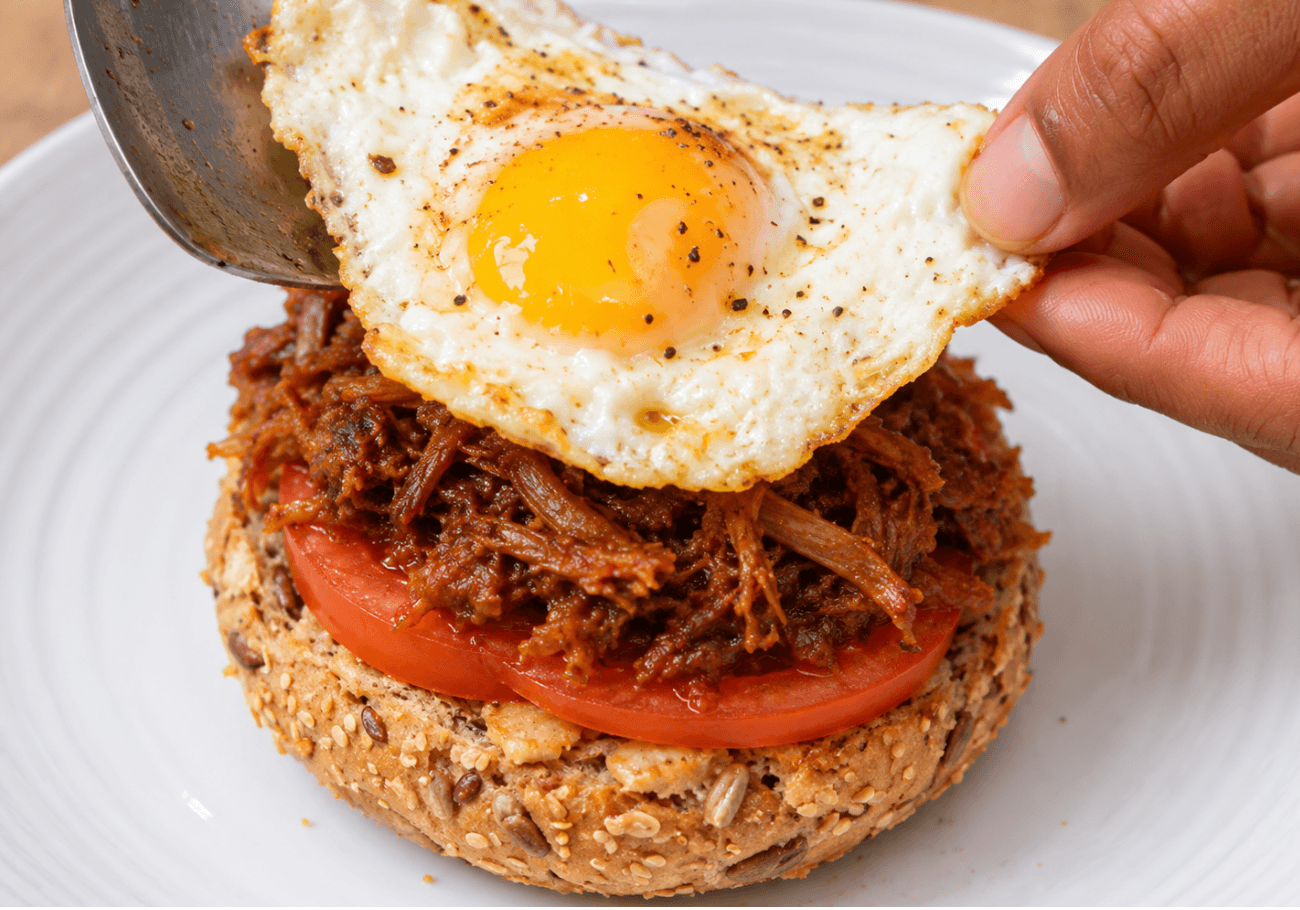 Fried egg placed over shredded duck and tomato for leftover duck sandwich