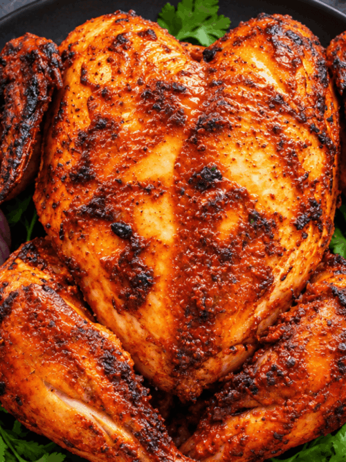 Restaurant style whole tandoori chicken plated with coriander, onion rings, and lemon wedges.