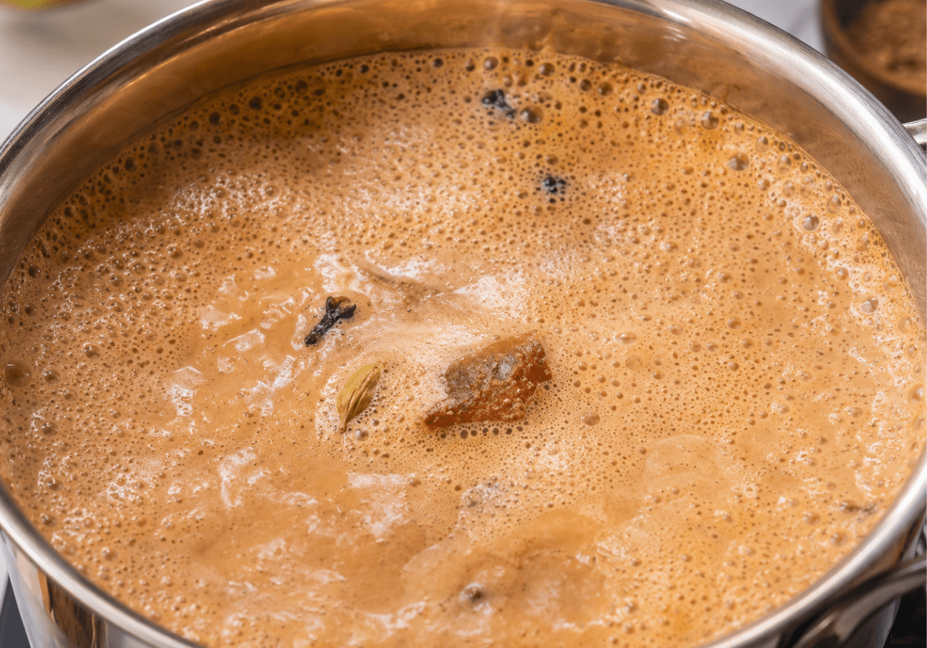 Masala tea recipe boiling in a steel pot with Indian spices